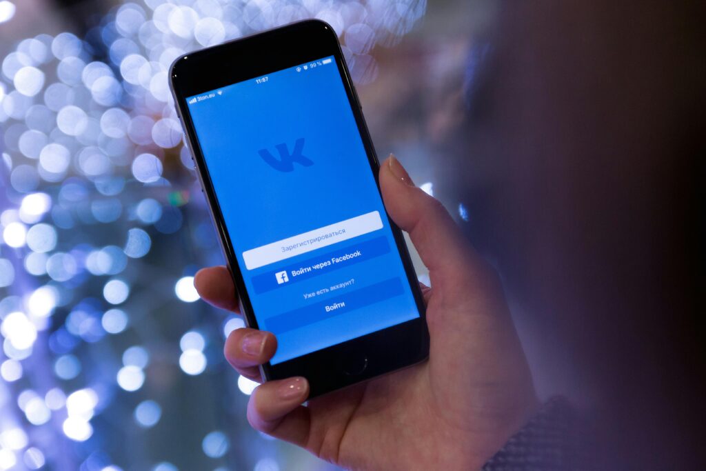 A hand holding a smartphone displaying the VKontakte app login screen.