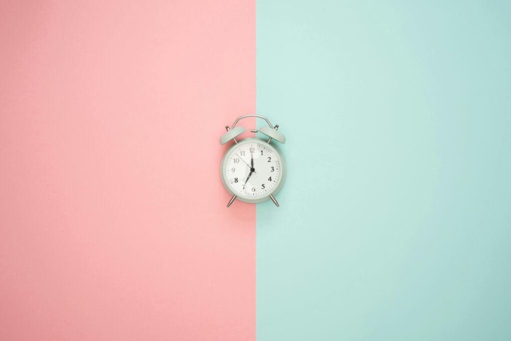 A vintage round clock on a split pastel pink and blue background.