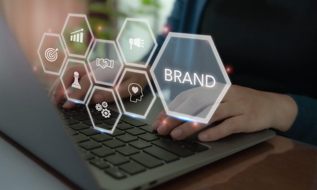 Hands typing on a laptop keyboard with floating hexagonal icons representing brand strategy and identity.